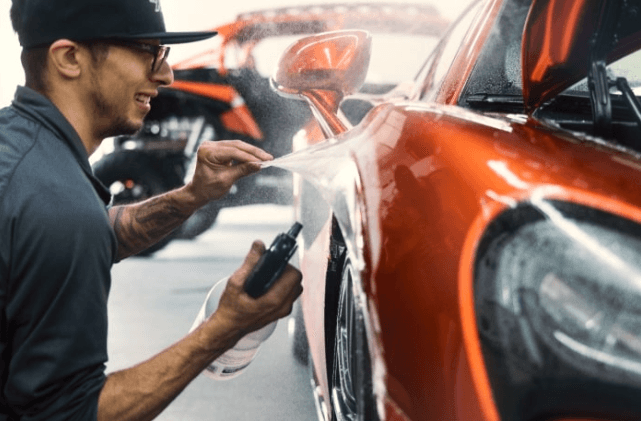 Professional automotive service technician working on orange sports car